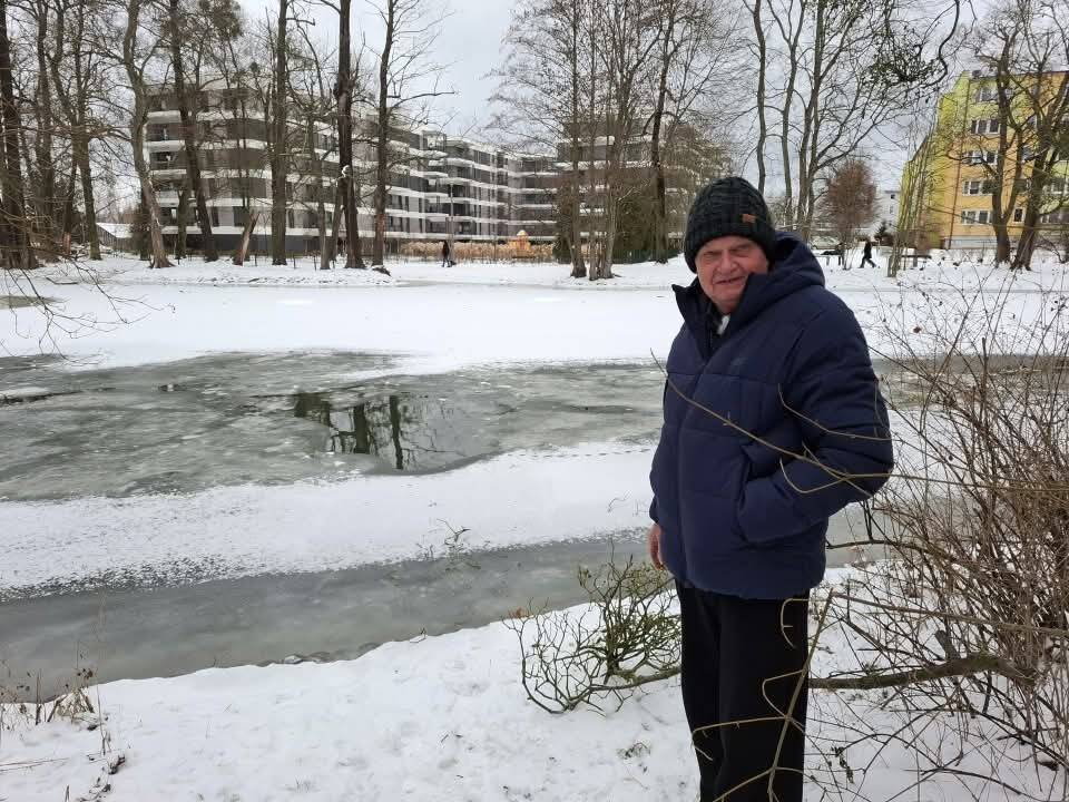 Człowiek w czapce i kurtce stoi na brzegu częściowo zamarzniętego Kanału Bydgoskiego